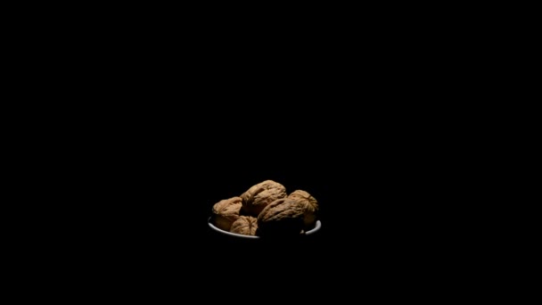 Плоды орехов грецкого ореха в белой чаше кружатся на черном фоне с сенитальным светом — стоковое видео