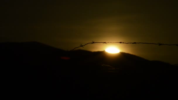 背景の山に隠れている太陽と有刺鉄線のフェンス — ストック動画