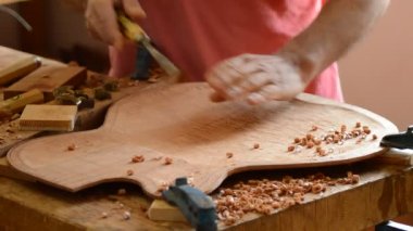 Luthier yeni bir gitarın kapağını küçük bir ahşap planörle zımparalıyor.