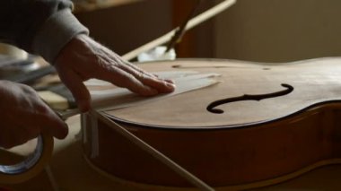Luthier bir caz elektro gitarının kutusunun kenarlarını sıkıştırıyor.