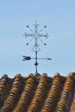Old cross-shaped weather vane next to old tiles of an old house