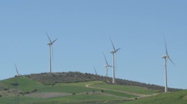 Tarladaki rüzgar türbinlerinin mavi gökyüzü ile hareket eden bıçakları.