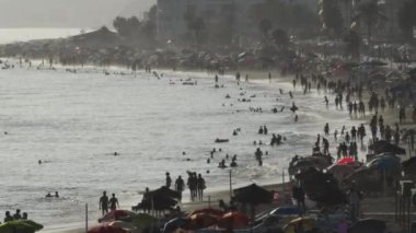 Gün batımında plaj dolusu insan ve şemsiye