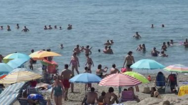 Akdeniz sahilinde güneşli bir günde insanlar plajda banyo ve şemsiye yapıyor.