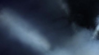 Bir konserde sahne ışıkları hareket ediyor ve duman çıkıyor.