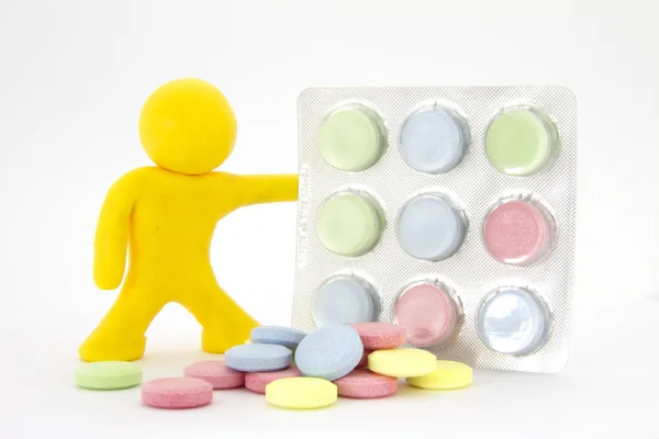 Caráter de plasticina amarela e comprimidos coloridos comprimidos na embalagem. Tema da farmácia. Isolado sobre fundo branco — Fotografia de Stock