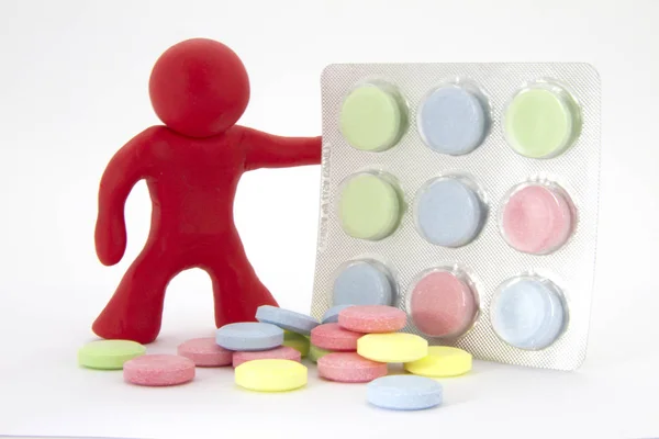 Caráter de plasticina vermelha e comprimidos coloridos comprimidos na embalagem. Tema da farmácia. Isolado sobre fundo branco — Fotografia de Stock