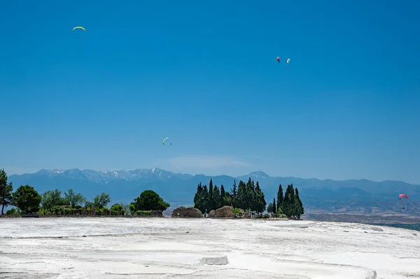 Türkiye 'nin özgür kenti Hierapolis' te Pamukkale 'nin kar beyazı Travertineleri üzerinde uçan paraşütçüler.