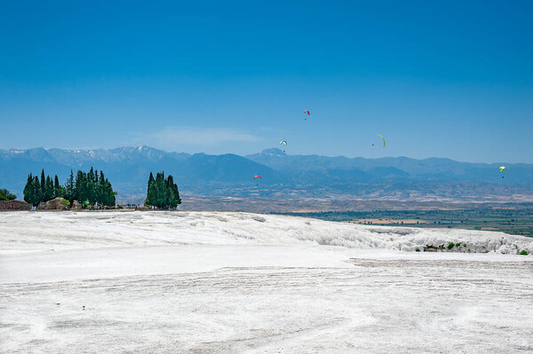 Paragliders flying above snow white Travertines of Pamukkale in anciet city of Hierapolis in Turkey.
