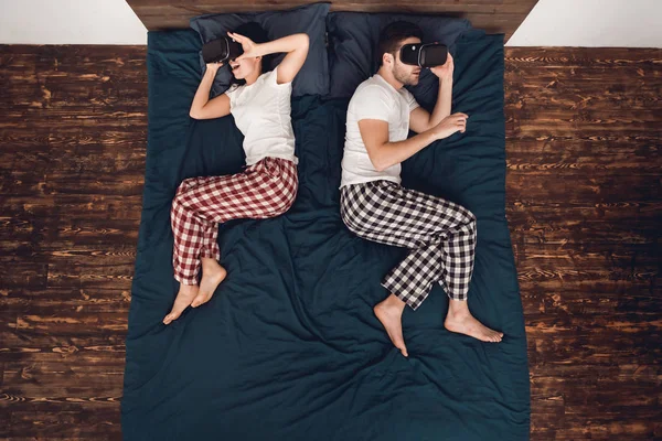 Ansicht von oben. junge Frau und Mann liegen auf dem Bett und schauen in eine Virtual-Reality-Brille. Freizeit zu Hause. — Stockfoto