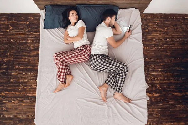 Vista do reboque. Homem bonito adulto com telefone nas mãos evita dormir ao lado de uma jovem deitada . — Fotografia de Stock