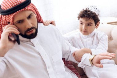 Little boy asks attention of busy Arab father. clipart