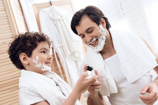 Joyful father inserts shaving foam onto hands of young son.