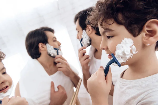 Bearded father with small son is shaving in bathroom.