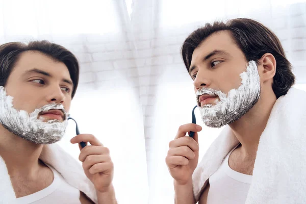 Bearded man neatly shaves beard in shaving foam.