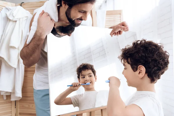 Fröhlicher Sohn putzt Zähne, schaut in den Spiegel, der Vater hält. — Stockfoto