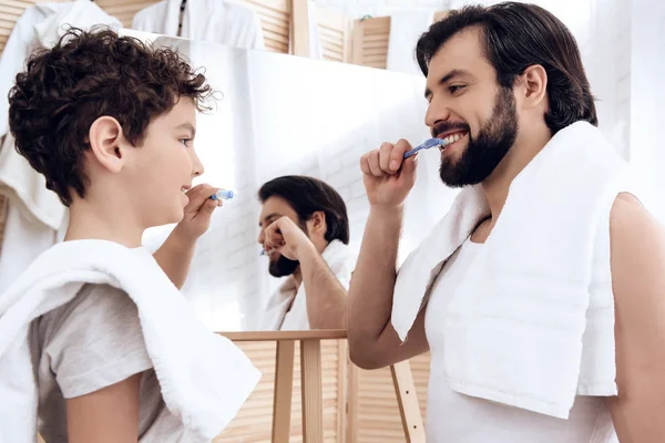 Feliz pai e filho escovar os dentes com escova de dentes, olhando no espelho . — Fotografia de Stock
