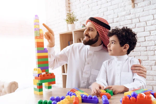 Arabische man met kleine jongen bouwt toren van gekleurde kunststof blokken. — Stockfoto