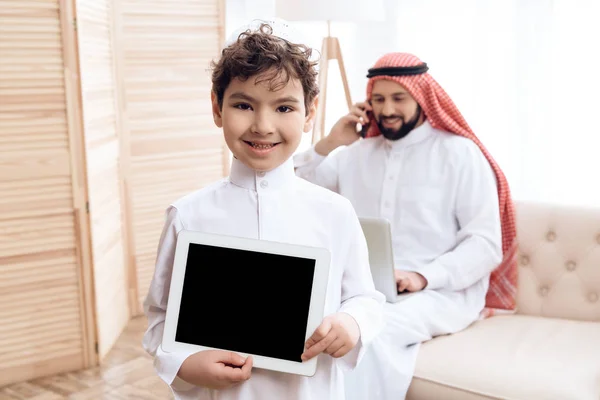 Joyful Arab boy looks at computer tablet while father works. — Stock Photo, Image