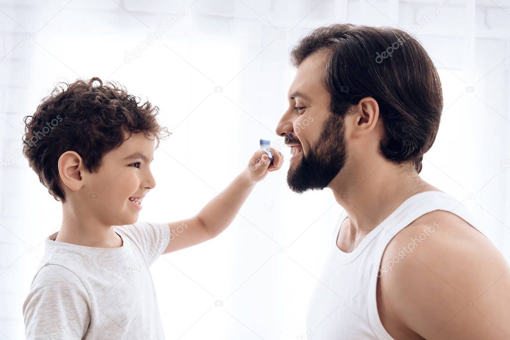 Little boy is brushing teeth of bearded man with toothbrush.