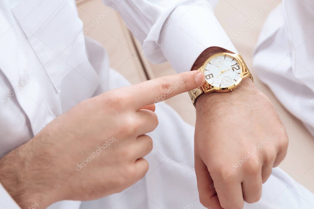 Close up. Man in white suit points y finger at golden watches.
