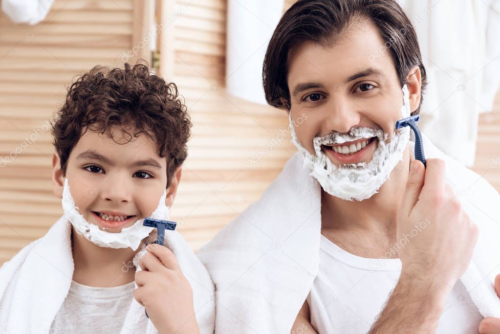 Portrait of father and son with razors which shaving in bathroom.