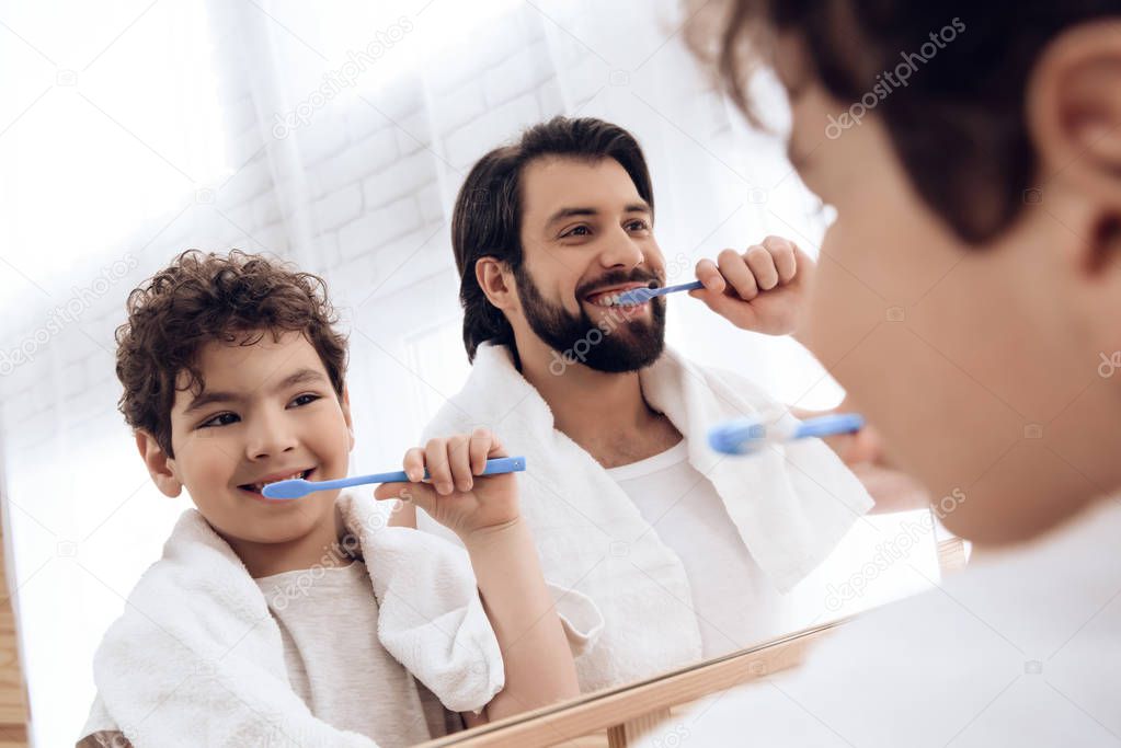 Happy father and son brush teeth with toothbrush, looking in mirror.