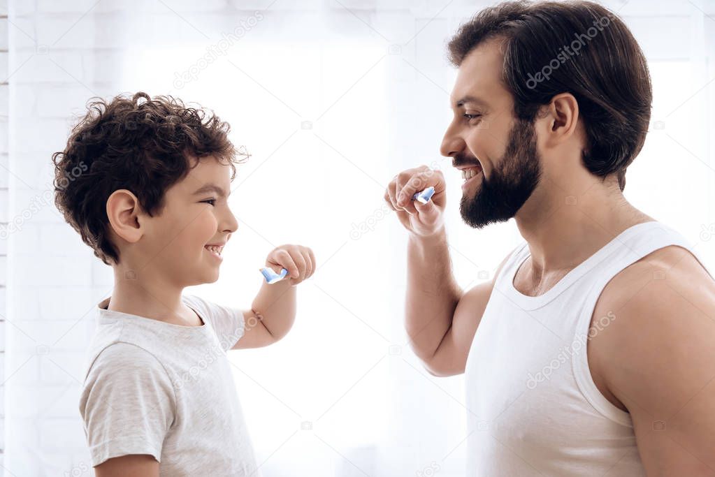Happy father and son brush teeth, looking at each other.