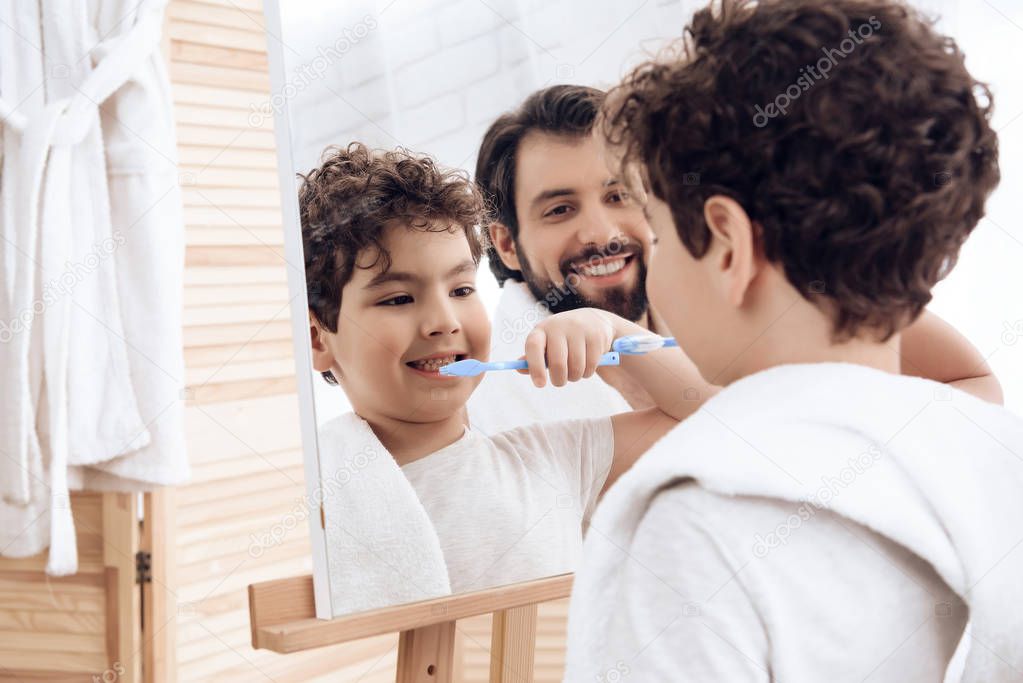 Happy father and son brush teeth with toothbrush, looking in mirror.