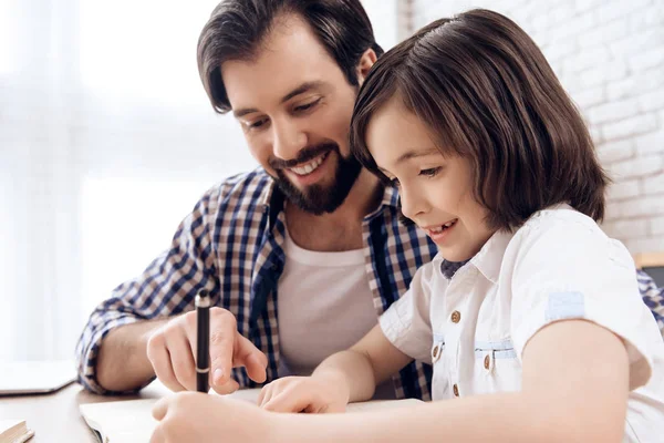 Padre barbudo ayuda a su hijo pequeño a hacer la tarea escolar . — Foto de Stock