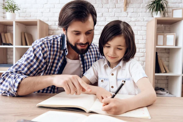 Padre barbudo ayuda a su hijo pequeño a hacer la tarea escolar . — Foto de Stock