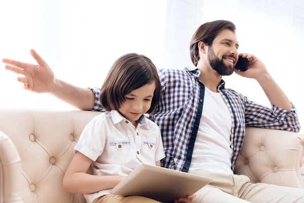 Happy boy is looking at computer tablet while father speaks on phone. — Stock Photo, Image