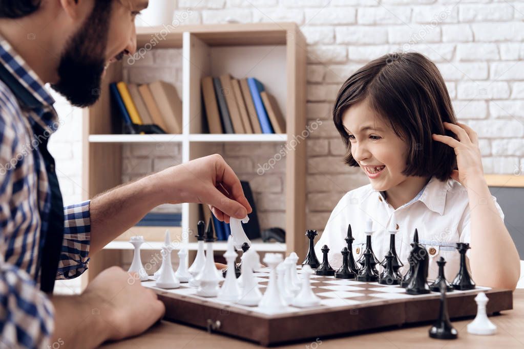 Happy bearded father plays chess with teenage son.