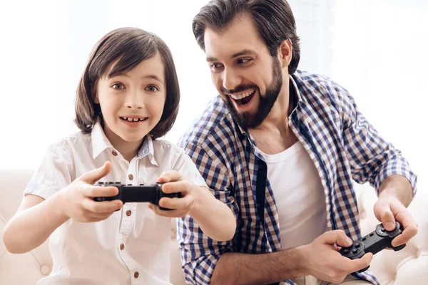 Bearded father with son plays computer game using game controllers.