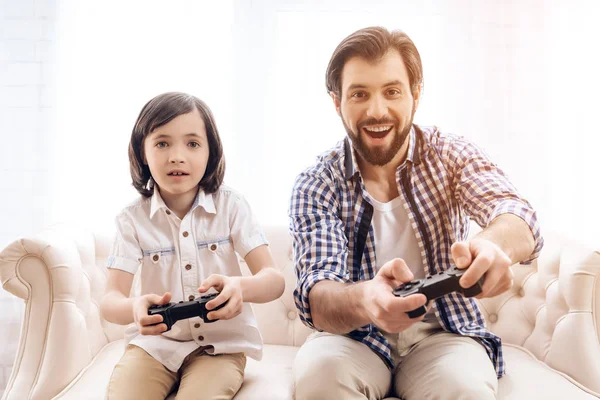 Bearded father with son plays computer game using game controllers.