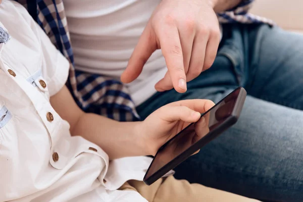 Close up. Adult man points to phone that is in boy\'s hands.