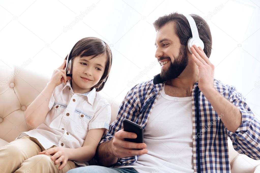 Bearded father and small son in headphones listen to music from smartphone.