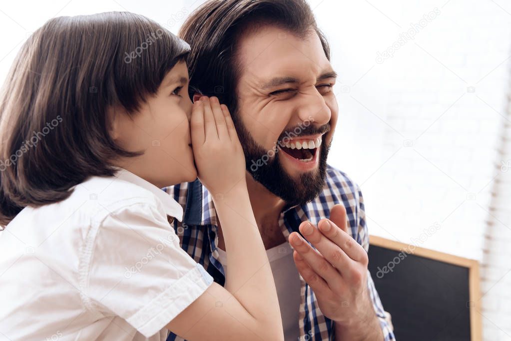 Small son speaks in ear of father a funny joke.