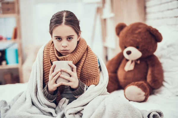 Menina com frio no lenço e cobertor com bebida quente nas mãos em casa . — Fotografia de Stock