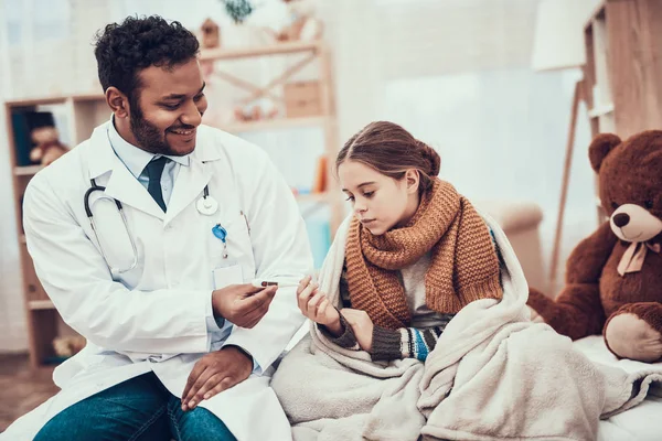 Indian doctor seeing patients at home. Doctor is taking temperature of little girl with cold.