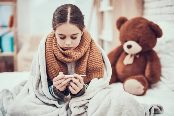 Menina com frio no lenço e cobertor com termômetro nas mãos em casa . — Fotografia de Stock