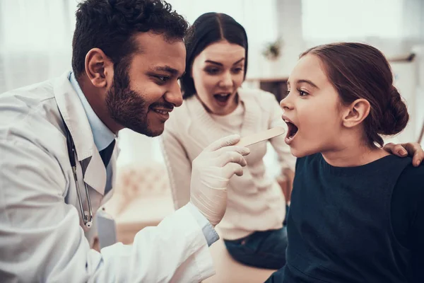 Indian doctor seeing patients in office. Doctor is examining daughter's throat.