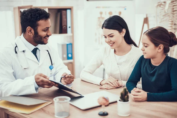 Médico indio viendo pacientes en el consultorio. Doctor está mostrando portapapeles a la madre y la hija . — Foto de Stock