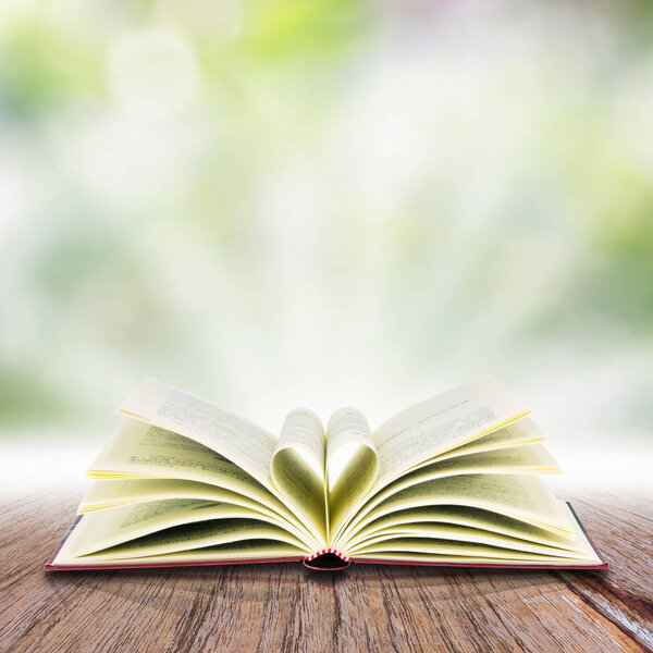 Open book on a wooden table , over abstract light background.