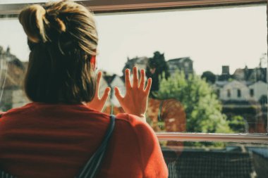 Pencereden dışarı bakan kadın elleri üzerine eğilmiş.