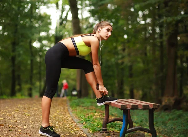 Kvinna med hörlurar gör fitnessövningar i park — Stockfoto
