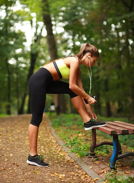 Kvinna med hörlurar gör fitnessövningar i park — Stockfoto