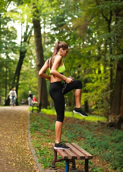 Kvinna med hörlurar gör fitnessövningar i park — Stockfoto