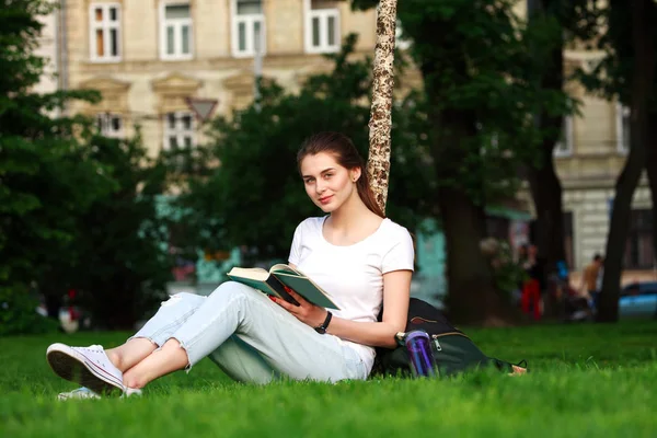 Chica sonriente estudiante en el parque de la ciudad con libro —  Fotos de Stock