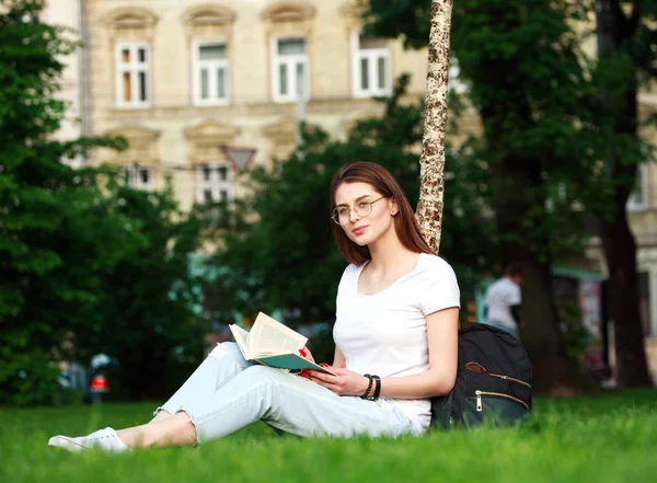 Estudante sorridente no parque da cidade com livro — Fotografia de Stock